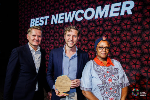 Emata CEO Bram van den Bosch (centre) accepts the award on stage in Copenhagen. On the right is the Ugandan ambassador to the Nordics and Baltics, and a Global Startup Award jury member to his left.